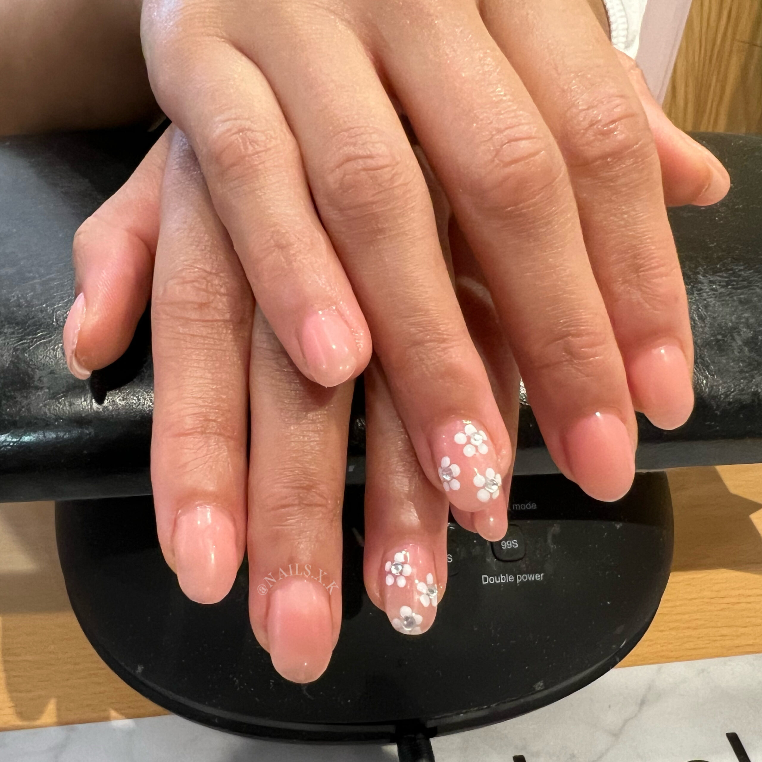 Hard gel set with a pink/nude color and floral designs with rhinestone accents. Nails by K