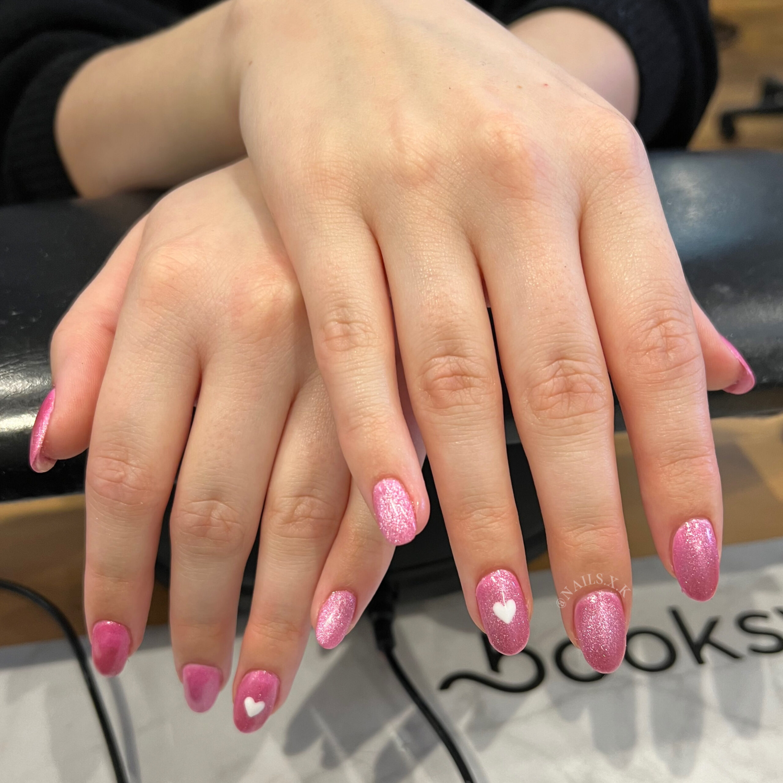 Acrylic nails with pink cat eye polish accented with white hand painted hearts. Nails by K