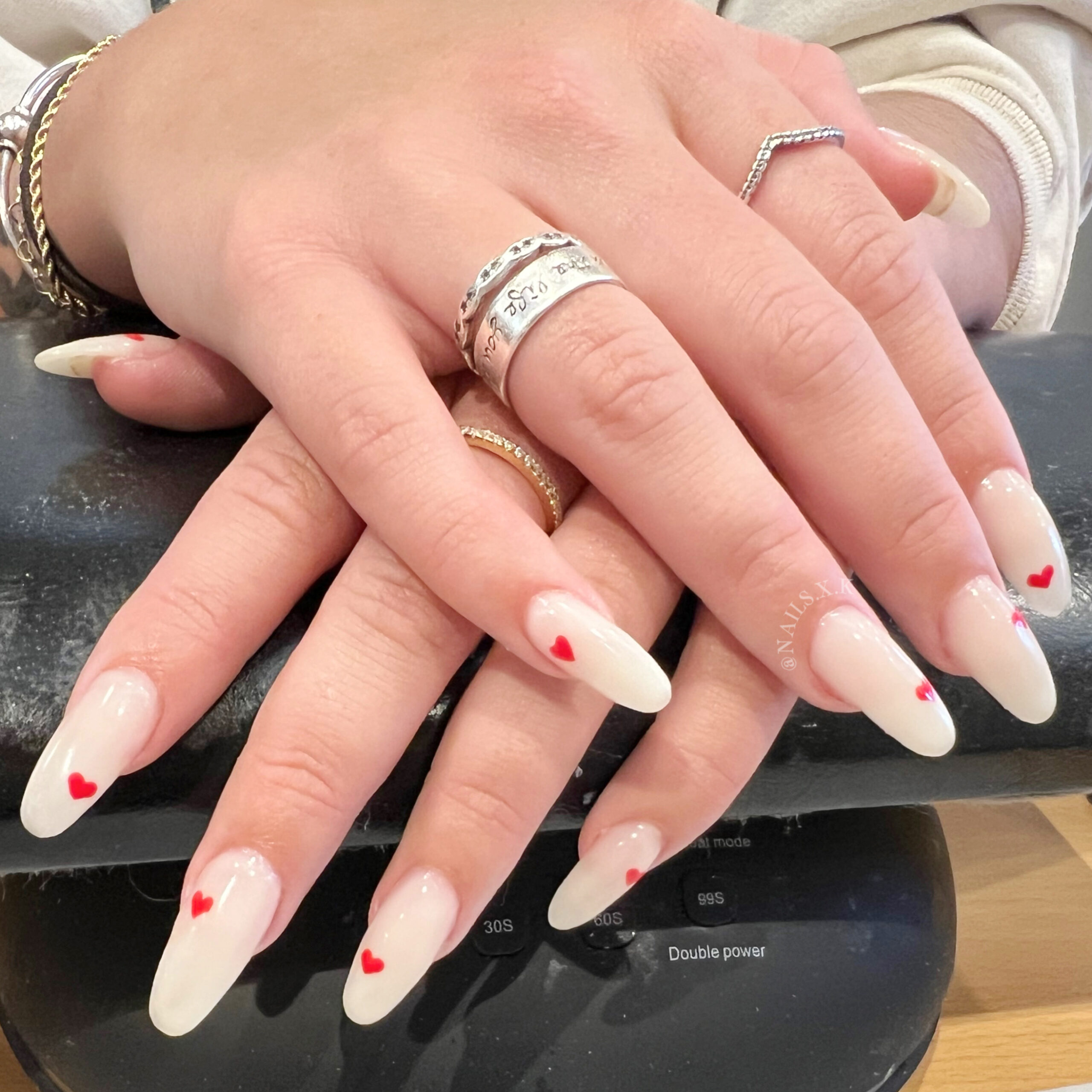 Acrylic nails with milky white color and tiny hand painted red hearts. Nails by K
