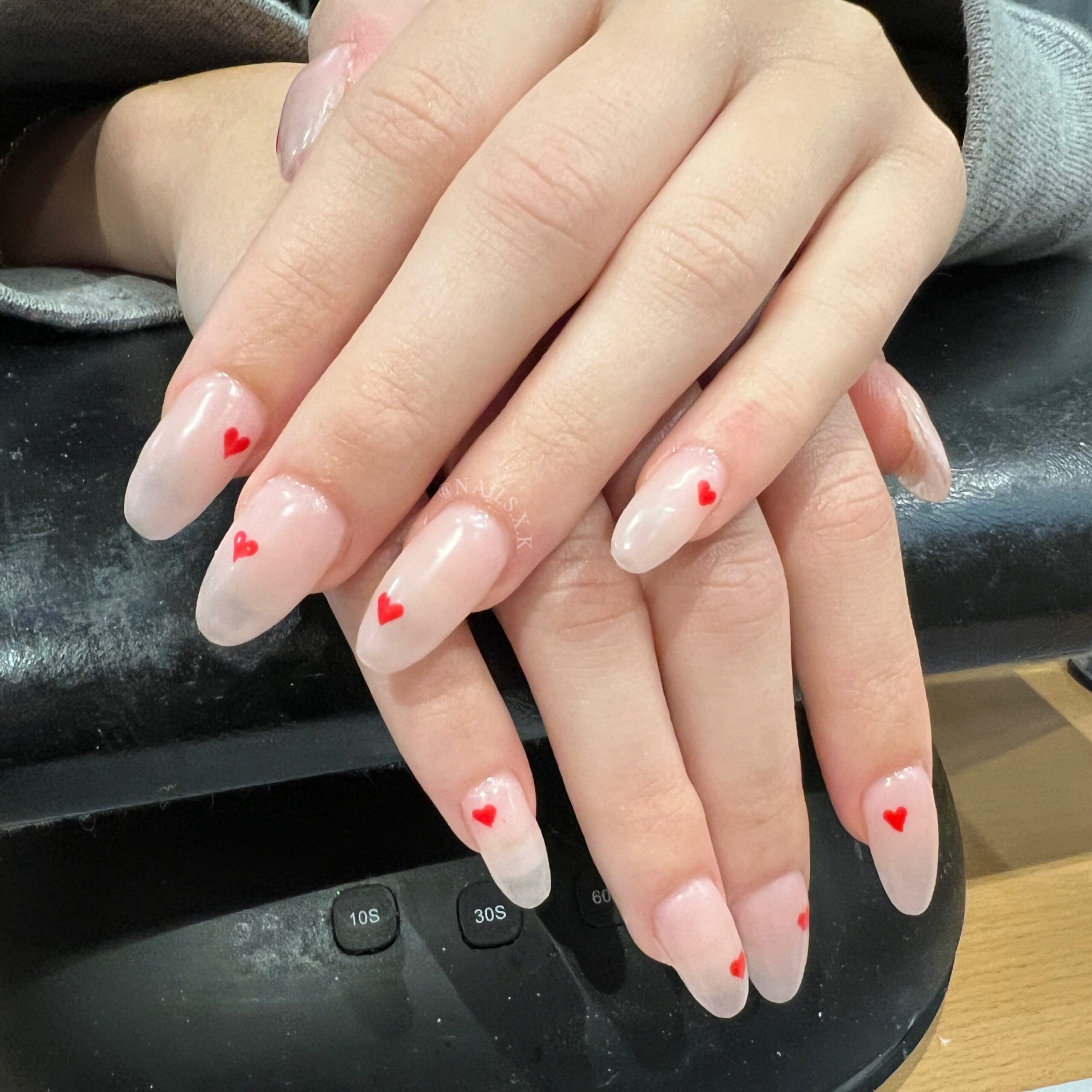 Acrylic nails with a nude pink color and red hand drawn hearts. Nails by K