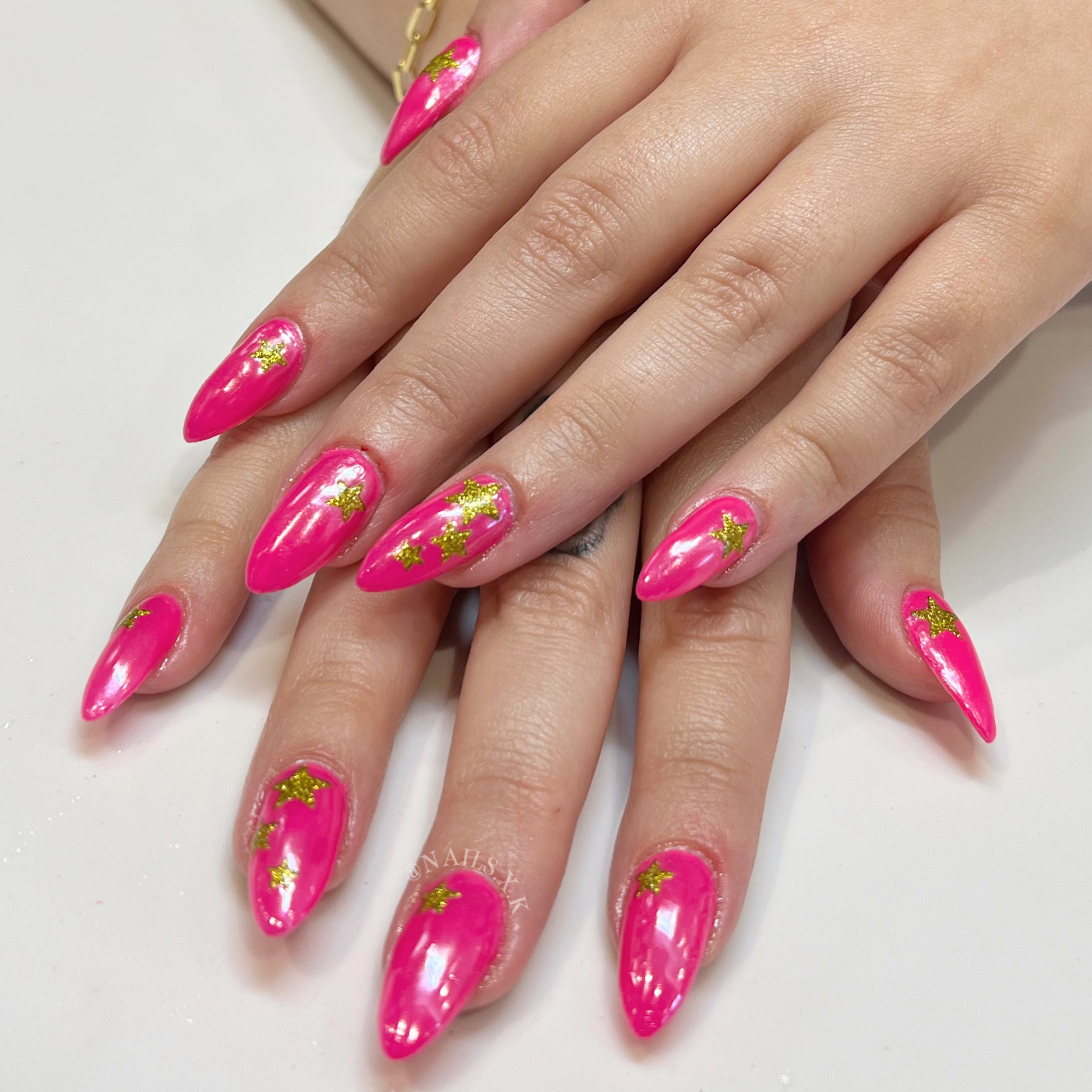 Hot pink acrylic nails with pearlescent chrome and gold glitter stars. Nails by K