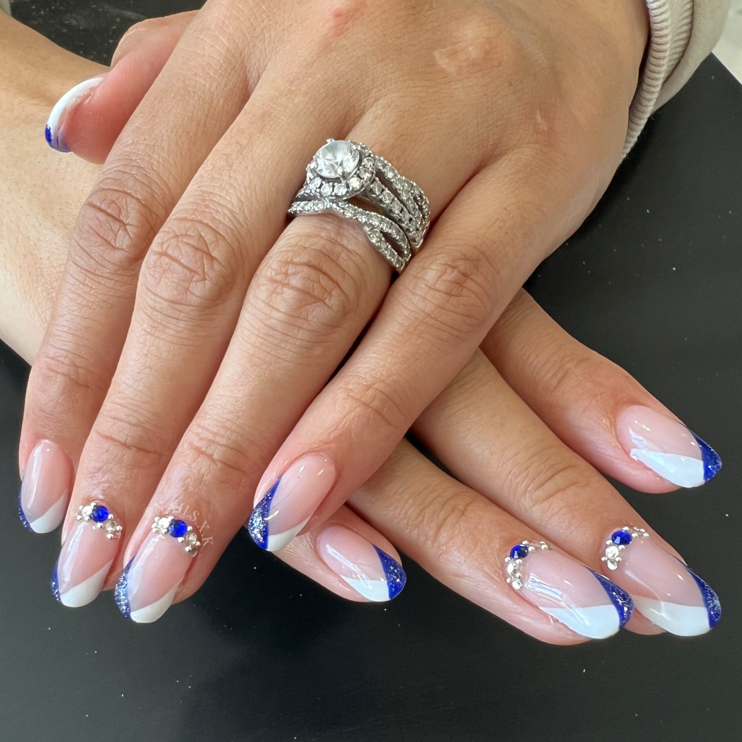 Hard gel nails with a deep blue and white french look accented with rhinestones. Nails by K