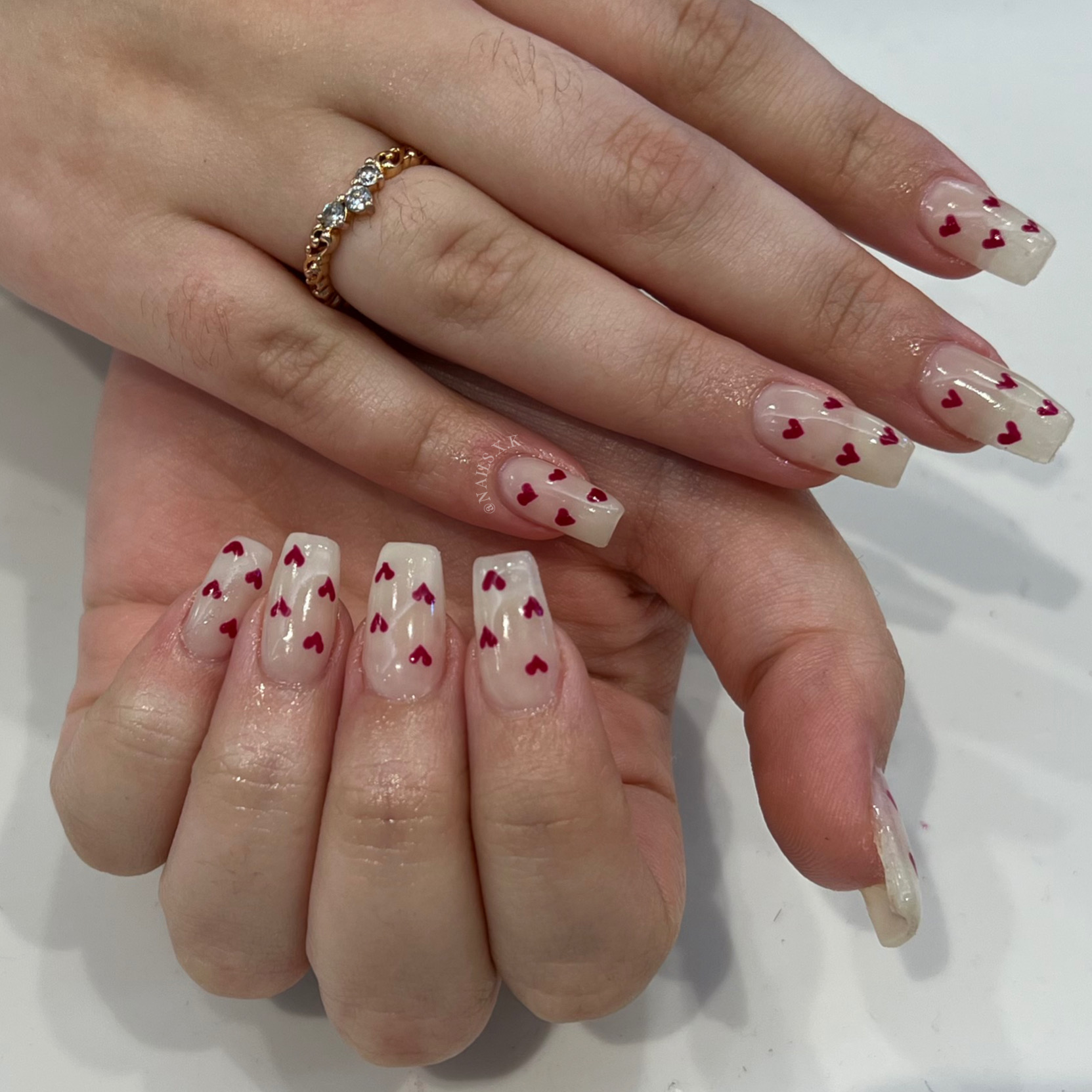 Hard gel nails with a creamy milky base and red hearts. Nails by K